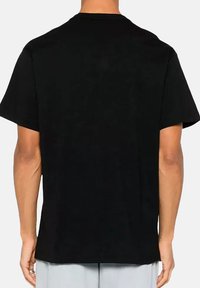 T-shirt in cotone nero con collo rotondo e maniche corte. La vista posteriore rivela una texture semplice e liscia, senza alcun motivo o grafica visibili.