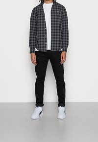 Rutig svart och grå skjorta med knappar, lager på lager över en vit t-shirt. Kombinerad med svarta jeans och vita sneakers med svarta accenter.