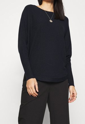 Marineblaues Pullover-Sweatshirt mit entspannter Passform, langen Ärmeln und einem strukturierten Strickmuster. Rundhalsausschnitt und Saum, getragen mit schwarzen Hosen.