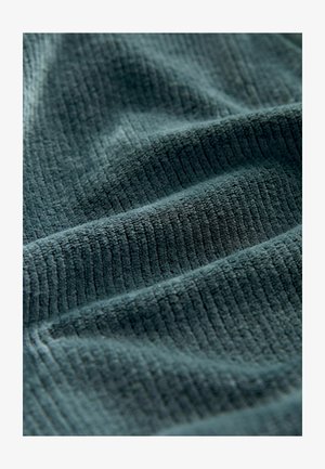 Țesătură texturată de un teal închis, cu un model vertical de nervuri. Suprafață moale și pufoasă, cu pliuri ondulate vizibile și accente de lumină.