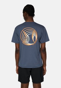 Mörkblå t-shirt i ett mjukt tyg, med ett cirkulärt geometriskt mönster i orange och krämfärg på baksidan. Korta ärmar, avslappnad passform.