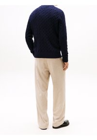 Pull en maille torsadée bleu marine, texturé, avec un col rond. Associé à un pantalon beige clair et des chaussures noires, présentant une coupe décontractée.