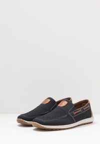 Scarpe slip-on con tomaia perforata blu navy, dettagli in pelle marrone e una suola bianca a contrasto con dettagli di cucitura.