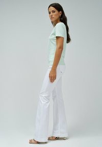 Camiseta de manga corta verde claro combinada con jeans acampanados blancos. El conjunto presenta un corte relajado y una textura de tela suave.