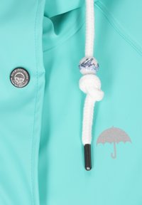 Mėtų žalios spalvos lietpaltis, su sidabro detalėmis, pintu baltu raišteliu ir dekoratyvine karoliukų puošmena su laivo raštu.