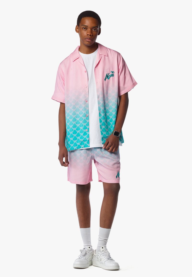 Ensemble short à manches courtes et shorts dégradés en rose et turquoise avec logo de palmier, tissu léger et motif subtil. Baskets portées.