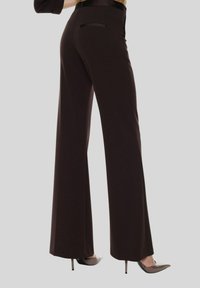 Pantaloni a gamba larga marroni realizzati in un tessuto liscio, con una tasca sul retro e abbinati a tacchi a punta, che mostrano una silhouette elegante.