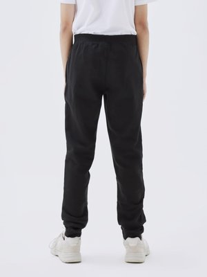 Black sweatpants with a ribbed waistband, elastic cuffs, and a relaxed fit, paired with white sneakers, viewed from the back.