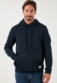 Felpa blu navy realizzata in morbido tessuto, con tasca frontale, cordini e una piccola etichetta logo sull'orlo. Design classico a pullover.