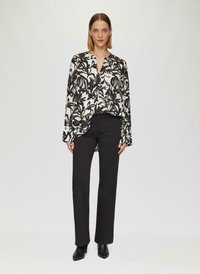 Zwart-witte bloemenpatroon blouse met een V-hals en lange mouwen, gecombineerd met zwarte rechte broek en haklaarzen.