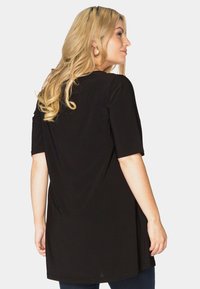 Sort tunika med korte ærmer, lavet af blødt stof. Har en afslappet pasform og rund kant. Bagsiden viser længden, der dækker hofterne.