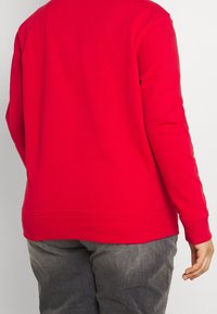 Rode sweatshirt met lange mouwen en ronde hals, met een gladde textuur en geribbelde manchetten, gecombineerd met grijze broek. De zoom is licht gebogen.