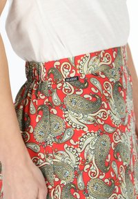 Gonna rossa a paisley con elastico in vita e etichetta nera "SEASIDE". Presenta dettagli intricati in blu e oro, con una texture liscia.