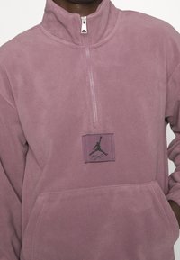 Fleece halvdraget tröja i ljuslila med en frontficka i kangaroo-stil och en svart Jumpman-logotyp på bröstet.