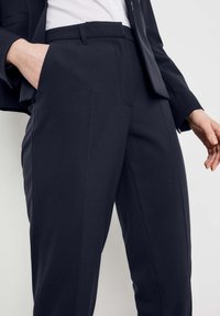 Granatowe spodnie casualowe z płaskim przodem, dwiema kieszeniami oraz gładką fakturą. Charakteryzują się dopasowanym krojem i subtelnym zagięciem na przodzie nogawki.
