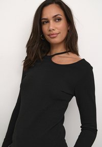 Schwarzes Langarmoberteil mit einem einzigartigen Ausschnitt an der Schulter. Hergestellt aus strukturiertem Material mit einem taillierten Design, das die Form und Silhouette betont.