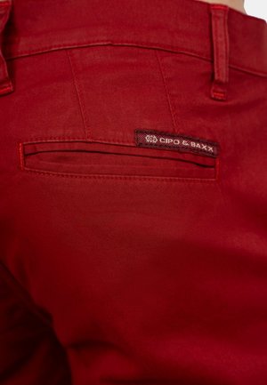 Red cotton pants with a smooth texture, featuring a back pocket and a branded label with "CIPO & BAXX." Stitching in matching red.