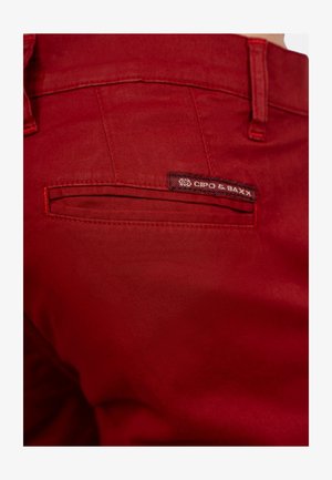 Rode katoenbroek met een gladde textuur, voorzien van een achterzak en een merklabel met "CIPO & BAXX." Stiksels in bijpassend rood.