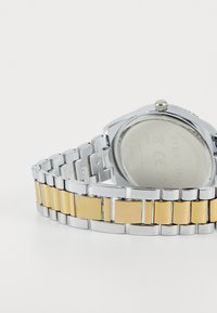 Montre-bracelet en acier inoxydable argent et or avec un cadran rectangulaire, design de bracelet à maillons, et un accent doré lisse sur certains maillons.