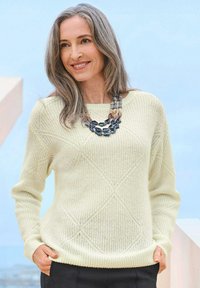 Hellgelbes gestricktes Sweatshirt mit einem Rautenmuster, gerippten Bündchen und einem geraden Saum. Kombiniert mit einer mehrfarbigen Statement-Halskette.