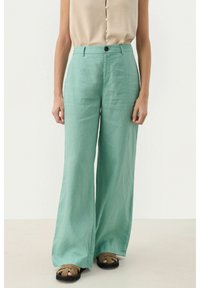 Pantalons en lin vert clair, à jambes larges, avec une taille haute et un unique bouton à l'avant. Tissu texturé avec une finition lisse.