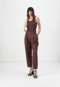 Brown tank top, high-waisted plum trousers with belt loops and a metal buckle, black heeled sandals, and a small beige handbag.
