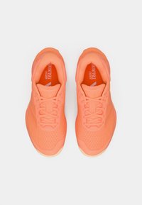 Πορτοκαλί-κοραλλί αθλητικά παπούτσια με υφασμάτινο επάνω μέρος με υφή, στρογγυλεμένη μύτη και επίπεδα κορδόνια. Εμφανές λογότυπο στη γλώσσα και στο πλάι.