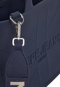Marineblå skuldertaske med præget logo, metalhardware og tekstureret rem med kontrasterende syninger.