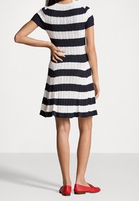 Randig stickad klänning i marinblått och vitt, med en figurnära överdel och utsvängd kjol. Kompletterad med röda platta skor.