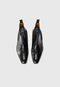 Botines de cuero negro con puntera puntiaguda, detalles decorativos de perforaciones, paneles laterales elásticos y un interior marrón en contraste.