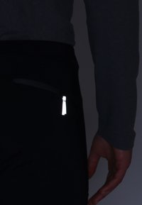 Pantalons de sport noirs avec des détails réfléchissants sur la fermeture éclair et un design ajusté, associés à un haut long manches gris.