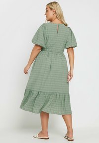 Vihreä ruudullinen midi-mekko, jossa on puffihihat, joustava vyötärö ja kerroksellinen röyhelöhame. Mekossa on takana avaus, jossa on avainreikä, sekä hienovarainen tekstuuri.