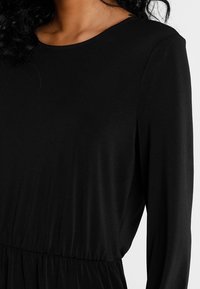 Svart långärmad klänning med rund halsringning, med en insydd midja och mjuk, slät tygtextur. Enkel och modern design.