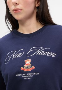 Granatowy sweter z haftowanym napisem "New Haven", logo z herbu oraz napisem "American Sportswear" poniżej. Miękka mieszanka bawełny, okrągły dekolt.