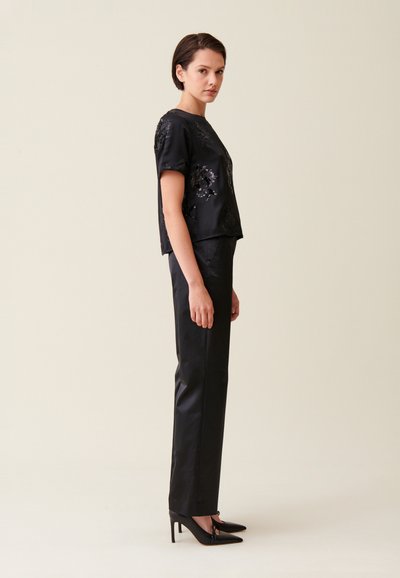 Top in raso nero con decorazioni floreali in paillettes, abbinato a pantaloni neri su misura e décolleté con punta affilata. Tessuto liscio e design aderente.