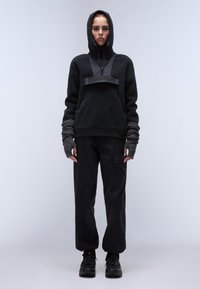 Sort fleece pullover med hætte, lynlås foran og grå ærmeaccent; iført med sorte cargo bukser og sort fodtøj.