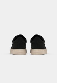 Adidași negri din pânză cu un design minimalist, având o textură netedă, vârf rotund și o talpă bej deschis. Fără branding vizibil.