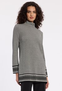 Zwart-wit gestreepte langesleeve top met hoge hals, voorzien van een geometrisch patroon en een contrasterende geprinte zoom.