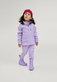 Veste imperméable violette avec une poche zippée, pantalons assortis et bottes en caoutchouc violettes. Un bonnet rose complète le look.