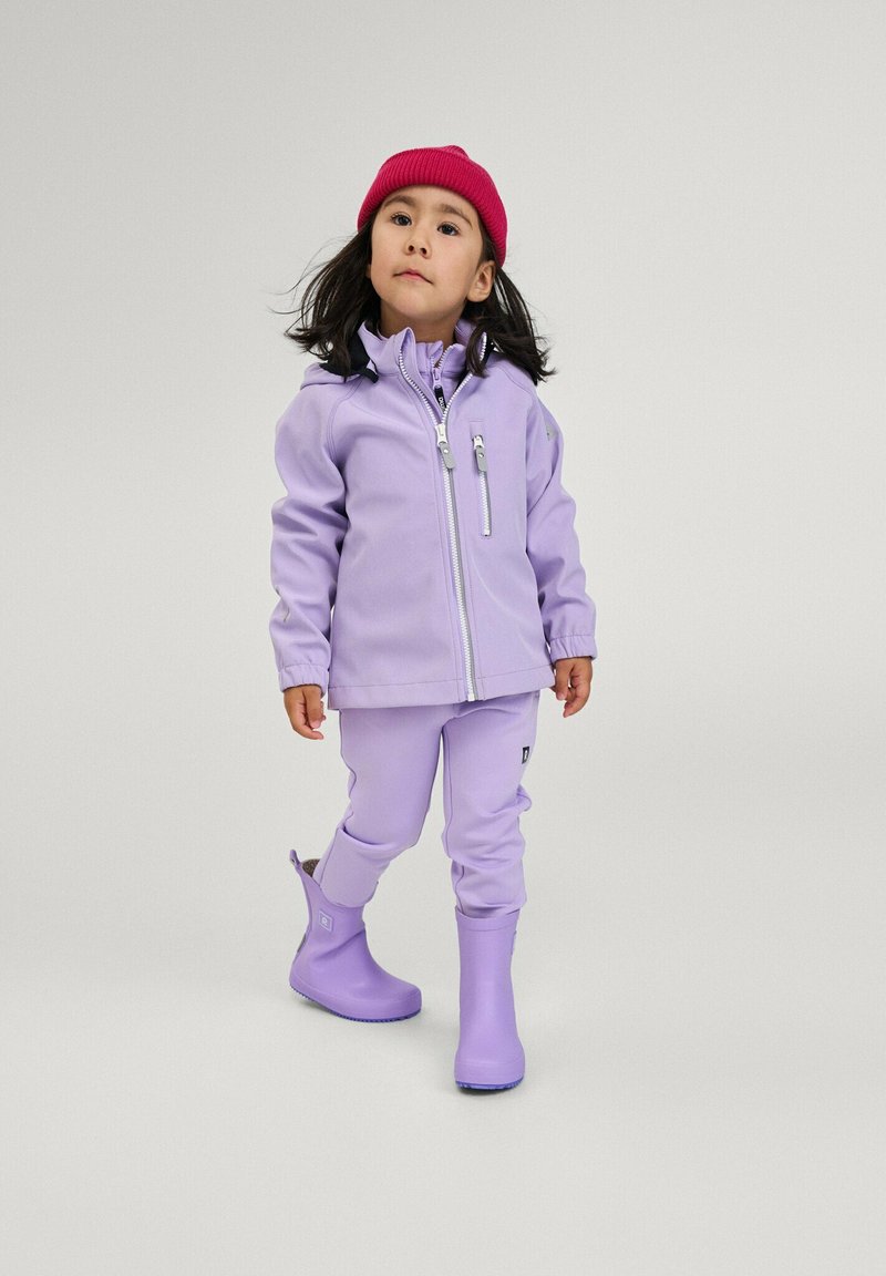 Veste imperméable violette avec une poche zippée, pantalons assortis et bottes en caoutchouc violettes. Un bonnet rose complète le look.