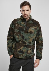 Sudadera de forro polar en un patrón de camuflaje con tonos marrones, verdes y negros; cuenta con un cierre de cuarto de cremallera en la parte delantera y un bolsillo en el pecho con cremallera.