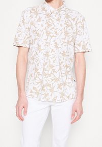 Polo a maniche corte in bianco e beige con un motivo floreale, dotato di colletto e orlo dritto.
