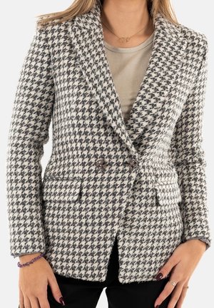 Woman wearing a black and white houndstooth blazer over a beige top, with black pants and purple bracelet on the left wrist.