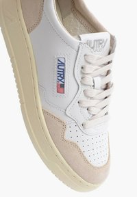 Scarpa da ginnastica in pelle bianca e beige con punta traforata, lacci color crema e marchio "Autry" con bandiera americana sul pannello laterale.