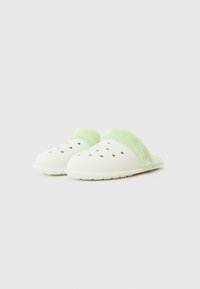 Ett par ljusgröna slip-on träskor med ventilationshål och mjuk foder runt öppningen på en vit bakgrund.