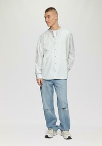Gestreepte button-up shirt in wit en lichtgroen, gecombineerd met lichtblauwe ripped jeans. Schoenen zijn lichtgrijs met donkere zolen.