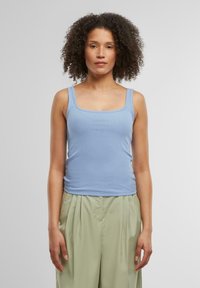 Top sin mangas de canalé azul claro con escote cuadrado, combinado con pantalones plisados verdes claros. Textura suave, diseño ajustado.