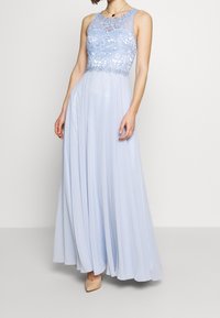 Světle modré večerní šaty s krajkovým živůtkem a květinovými vzory, splývavou šifonovou sukní. Bezramenný design s kulatým výstřihem.
