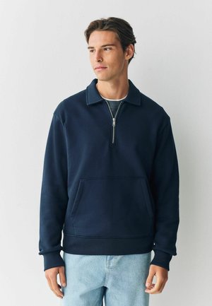 Navy blue fleece pullover with a zippered collar, front pocket, and ribbed cuffs. Features a relaxed fit and soft texture.