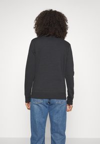 Svart sweatshirt med långa ärmar, ribbade muddar och fåll. Kombinerad med löst sittande blå denimjeans. Ren, minimalistisk design.